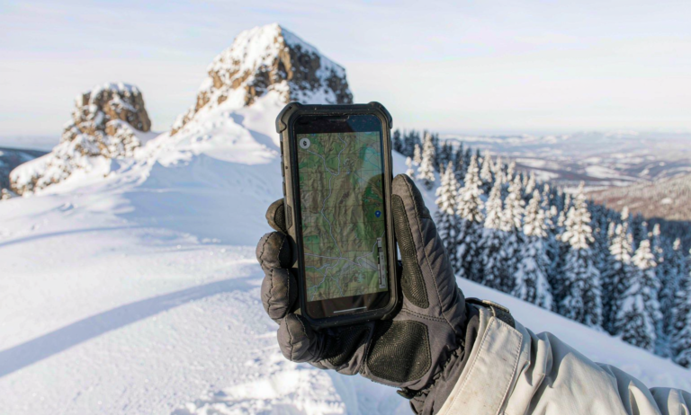 A gloved hand holding a phone showing a GPS offline map on an Altai backcountry ski slope